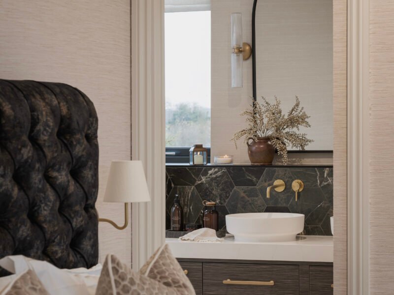 Calm bedroom with neutral tones, textured bedding, and an en suite vanity featuring natural materials and warm brass details