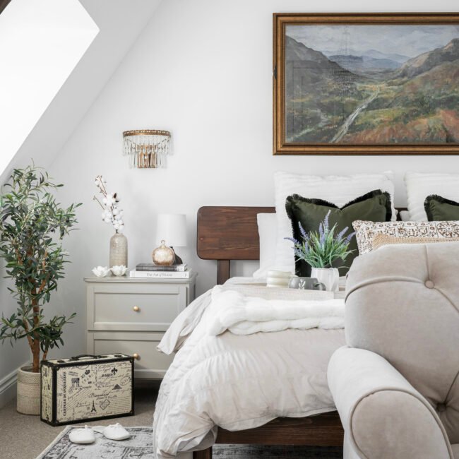 Calm, neutral bedroom designed by Maricruz Interiors in Bristol featuring layered soft textiles, olive green cushions, wooden bed frame, and thoughtfully styled bedside table.
