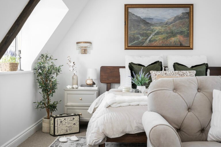 Calm, neutral bedroom designed by Maricruz Interiors in Bristol featuring layered soft textiles, olive green cushions, wooden bed frame, and thoughtfully styled bedside table.