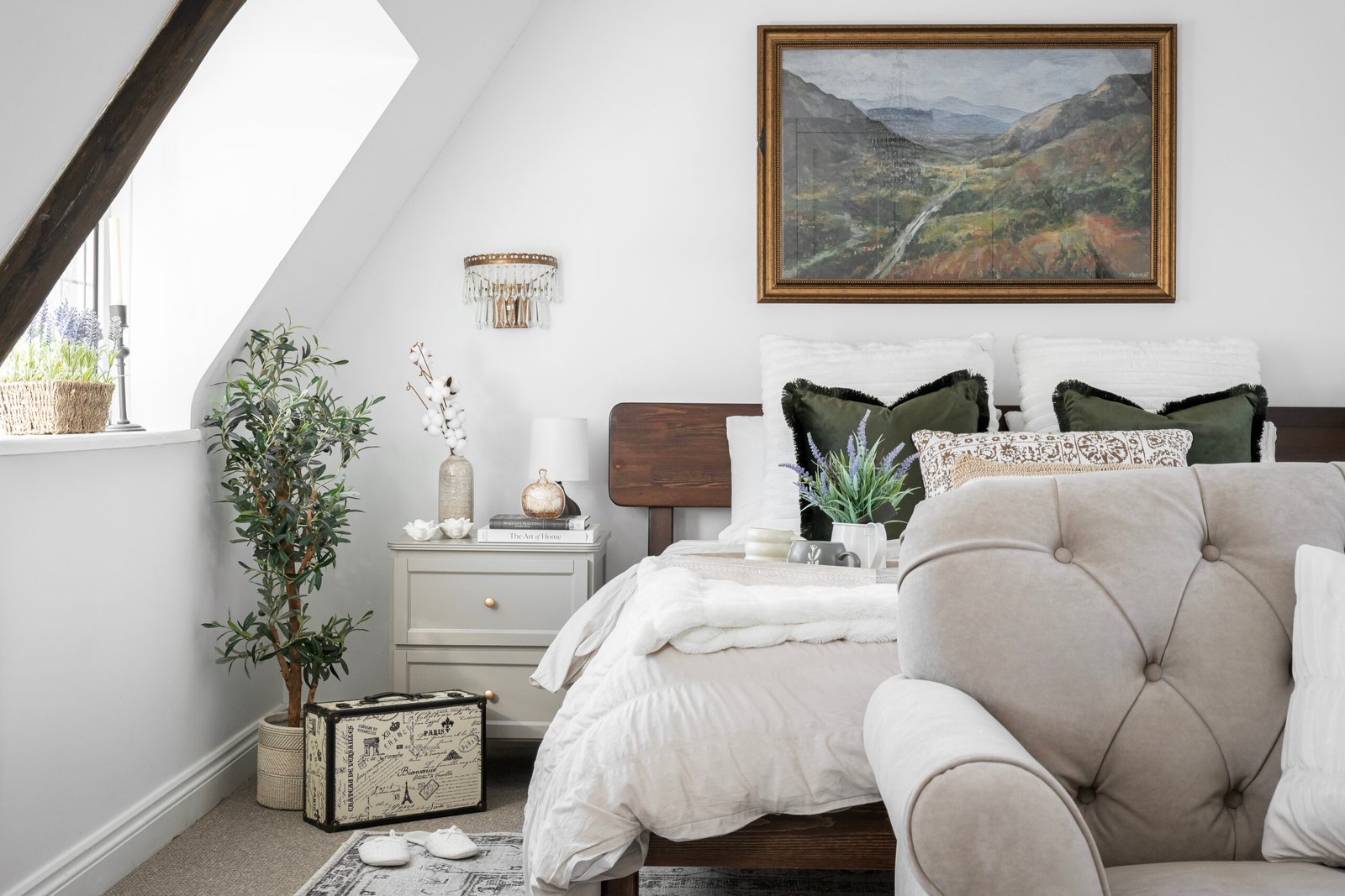 Calm, neutral bedroom designed by Maricruz Interiors in Bristol featuring layered soft textiles, olive green cushions, wooden bed frame, and thoughtfully styled bedside table.